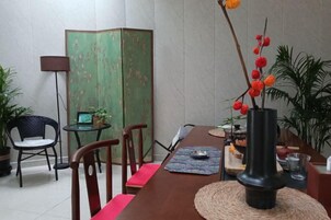 Un comedor con mesa de madera, sillas, un jarrón con flores rojas y un separador verde.