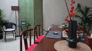 A dining area with a wooden table, chairs, a green cabinet, and a potted plant with orange flowers. - Shiguangli Inn (Suzhou)