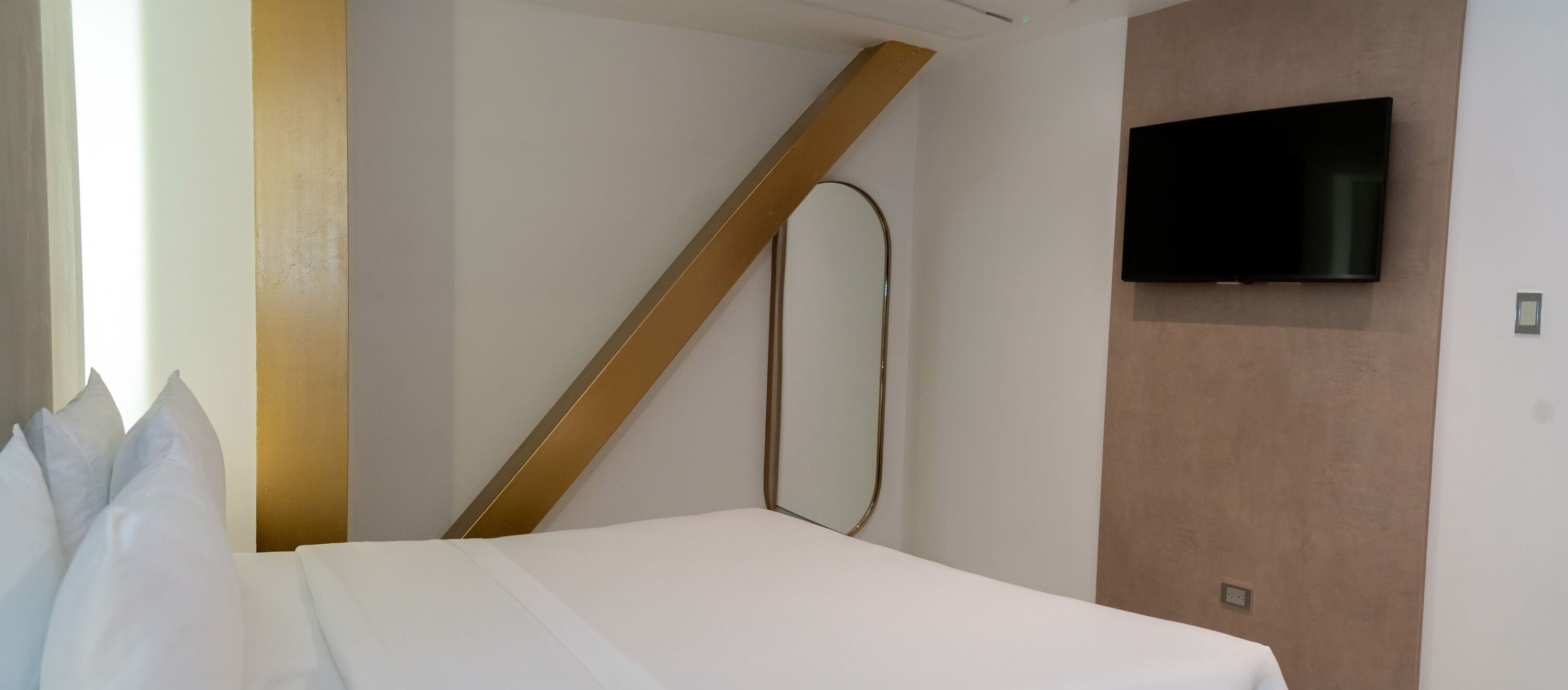 Een hotelkamer met een bed, een aan de muur bevestigde televisie en een groot raam.