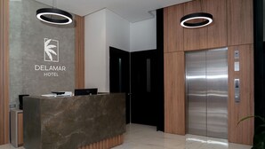 Zona de recepción de un hotel moderno con un mostrador de mármol, un logotipo en la parte superior y un panel de madera vertical.