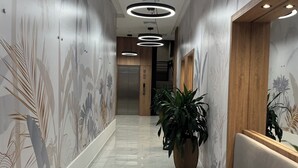 Un pasillo con suelo de mármol, una planta grande en maceta y un banco.