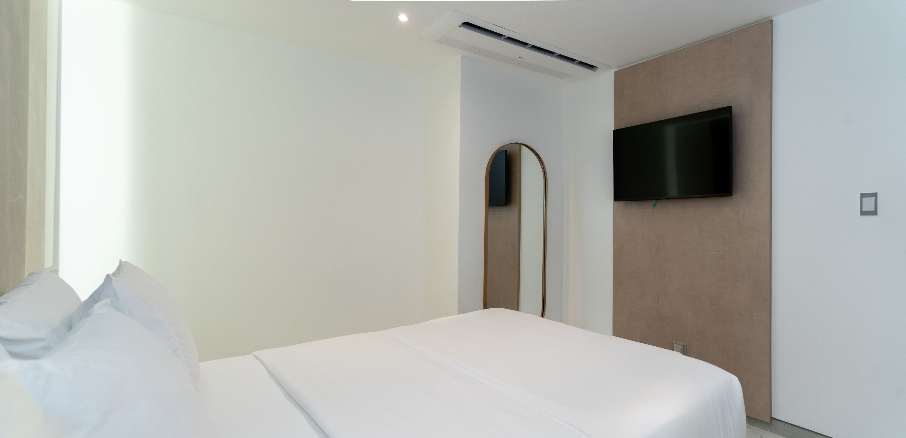 A modern hotel room with a bed, a flat-screen TV mounted on the wall, and a large mirror.
