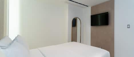 A modern hotel room with a bed, a flat-screen TV mounted on the wall, and a large mirror.