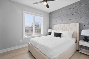 A bedroom with a large bed, a ceiling fan, a window with blinds, and a wall with zebra-patterned wallpaper. - Charlotte Luxury Townhomes (Charlotte)