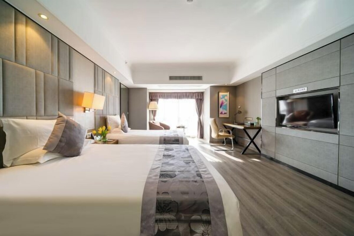Ein Hotelzimmer mit einem großen Bett, einem Schreibtisch, einem Fernseher und einer Küchenzeile.