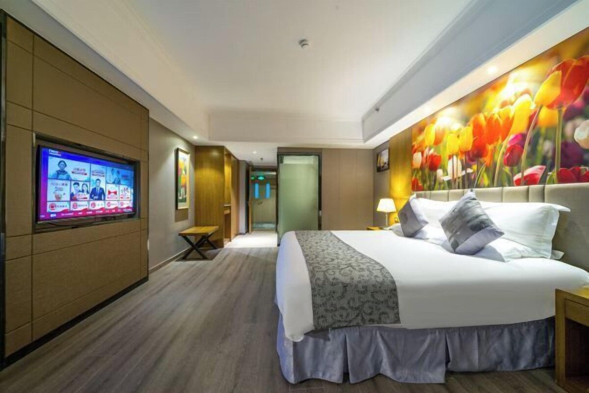 Ein Hotelzimmer mit einem großen Bett, einem an der Wand montierten Fernseher und einem floralen Wandbild.