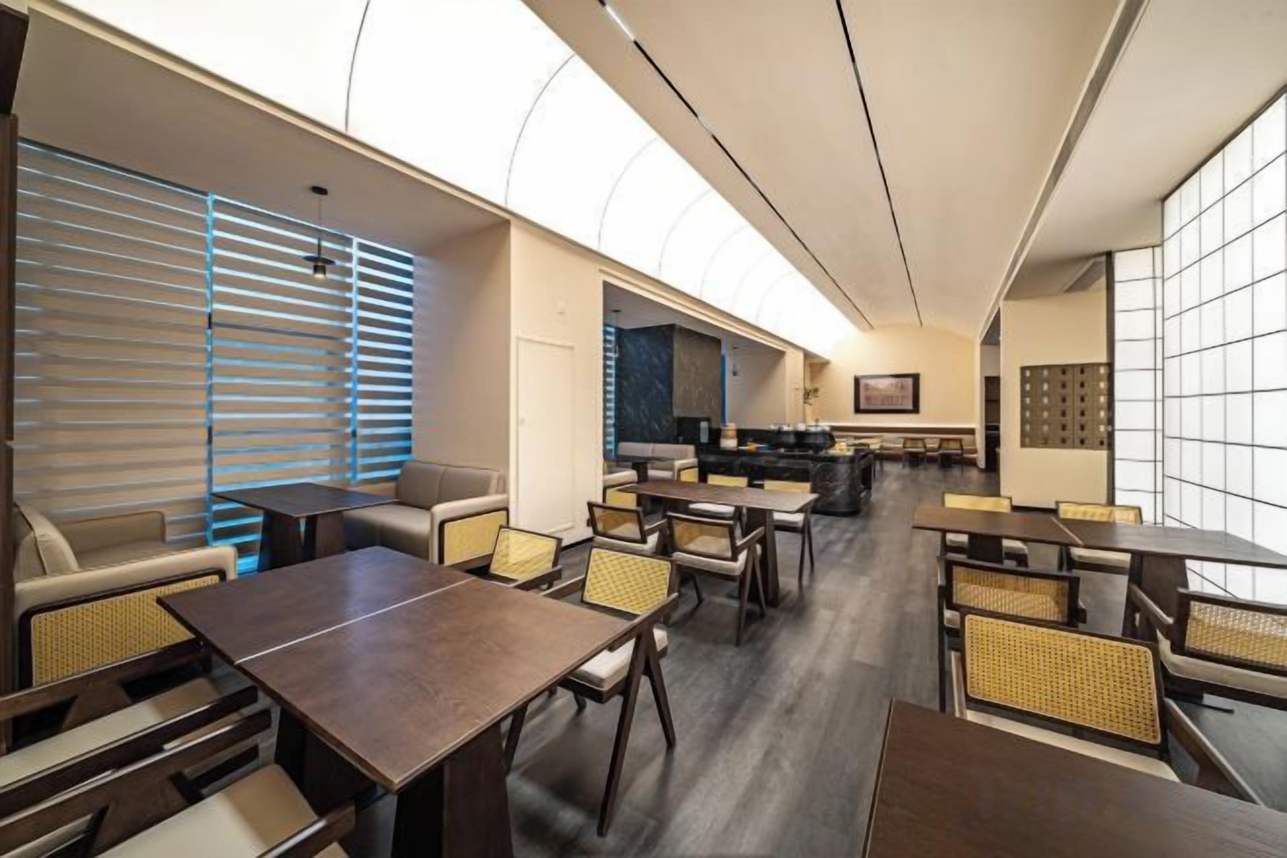 Un moderno vestíbulo de hotel con zona de comedor, asientos y una cocina al fondo.