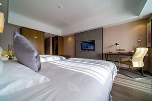 Ein Hotelzimmer mit einem großen Bett, einem Schreibtisch mit Stuhl, einem Fernseher und einem kleinen Tisch mit Blumen.
