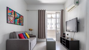 Un salon moderne avec un canapé gris, des coussins colorés, un téléviseur à écran plat et un meuble de rangement noir pour les appareils multimédias.