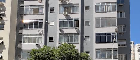 A multi-story building with a pharmacy on the ground floor, air conditioning units, and a tree in front.