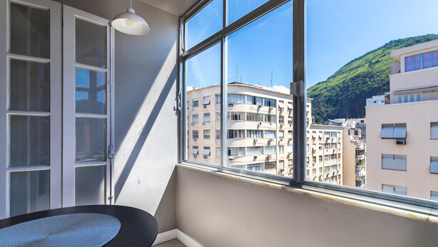 Une pièce avec une grande fenêtre, une chaise noire et un mur blanc.