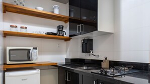 Une cuisine moderne avec des meubles de rangement noirs et blancs, un four à micro-ondes encastré, une machine à café et un petit réfrigérateur.