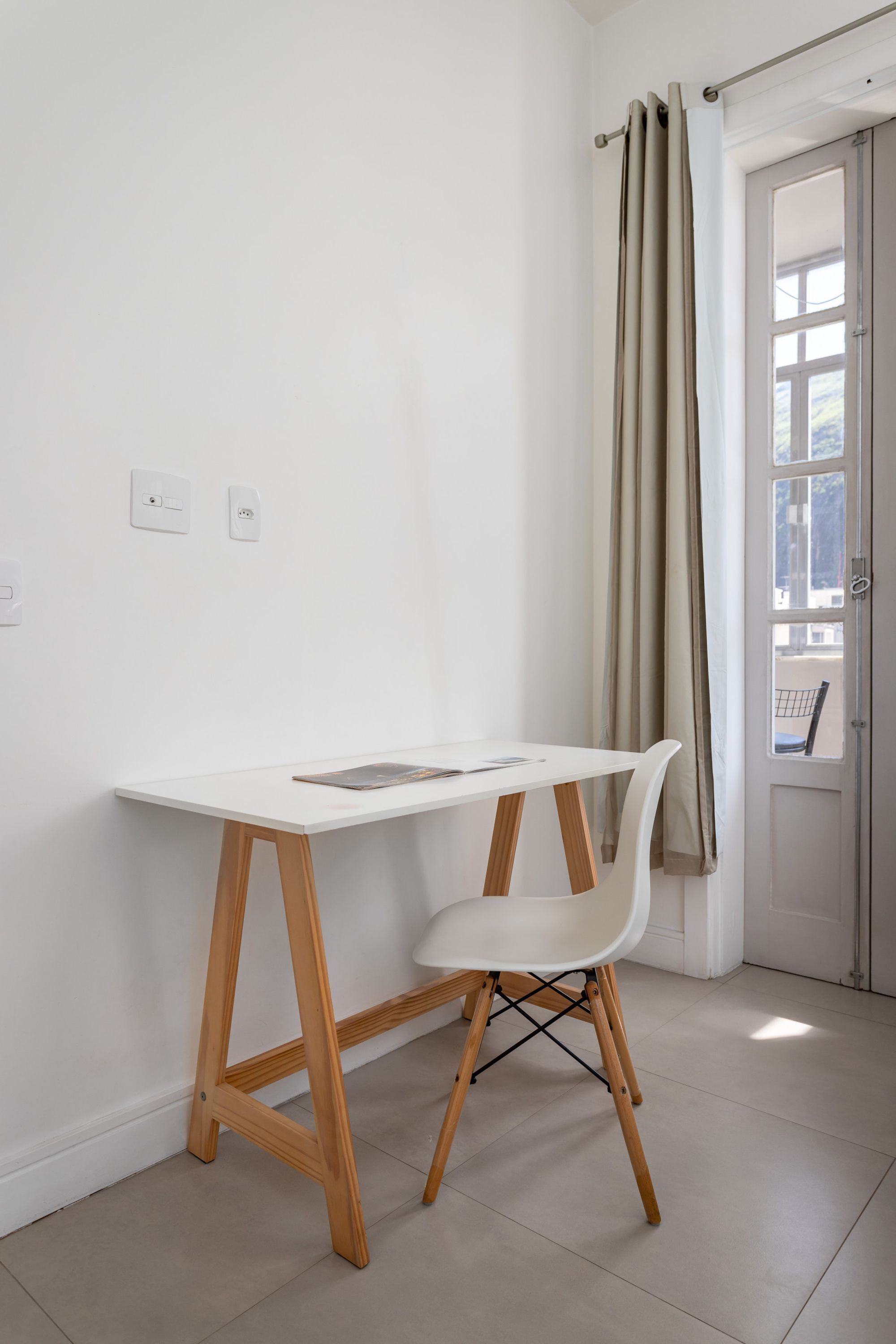 A minimalist room with a white desk and chair, a window with curtains, and a door.