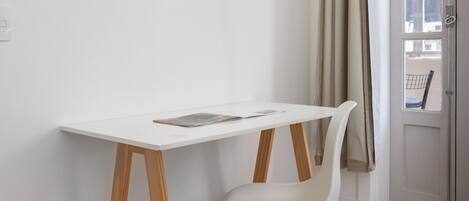 A minimalist room with a white desk and chair, a window with curtains, and a door.