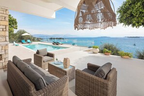 A poolside area with wicker furniture, a hanging macrame light, and a view of the sea. - Villa Dell Amore - Private dock - Private Pool - Seafront (Corfu)