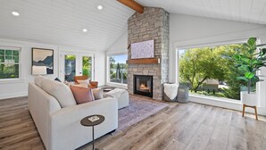 Una sala de estar moderna con chimenea de piedra, un ventanal con vistas a zonas verdes y un rincón de descanso acogedor.