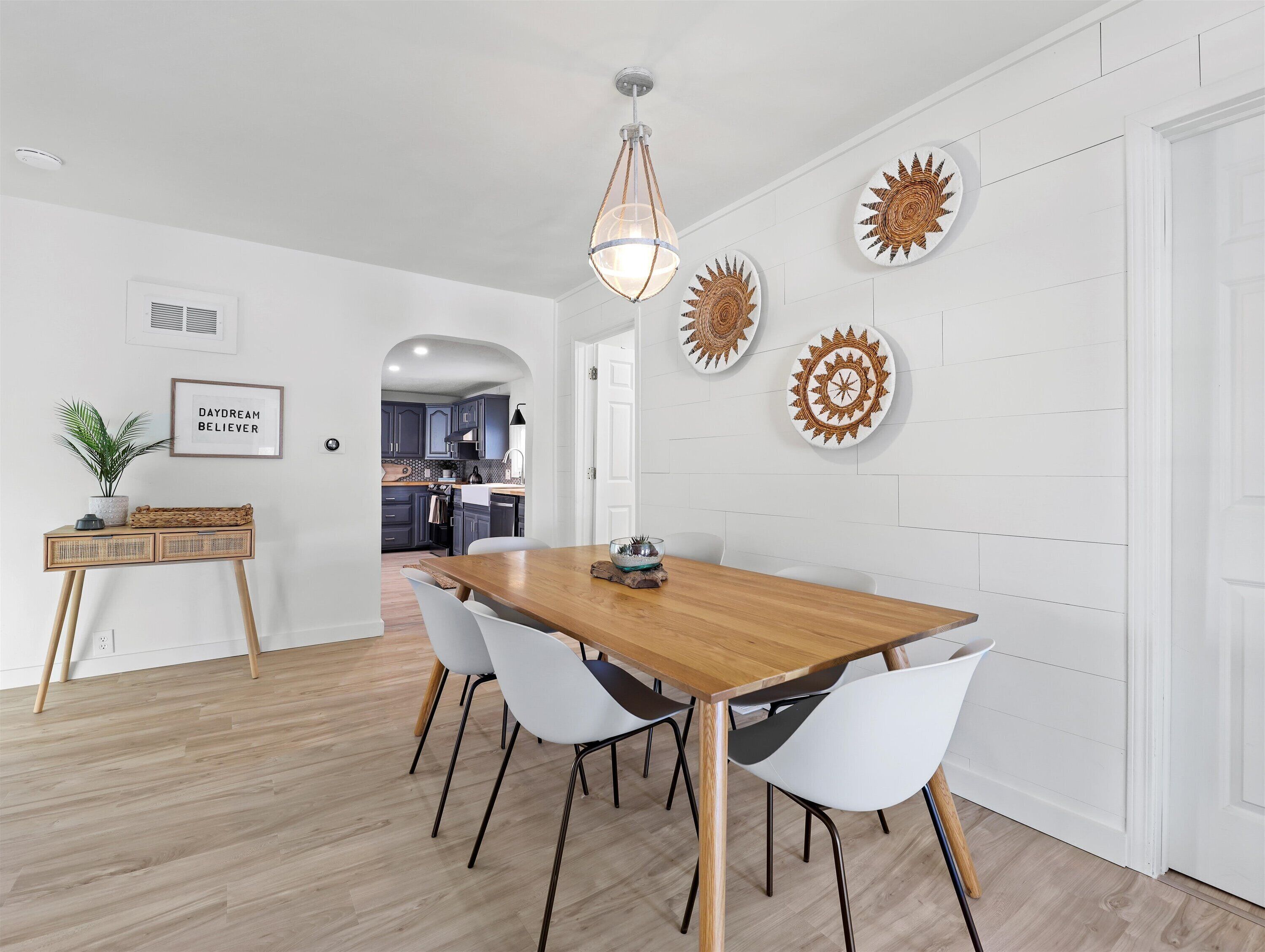 Un espace de salle à manger moderne avec une table en bois et des chaises blanches, un luminaire suspendu et des œuvres d’art décoratives au mur.