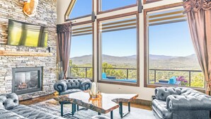A spacious living room with a stone fireplace, leather sofas, and large windows offering a mountain view.