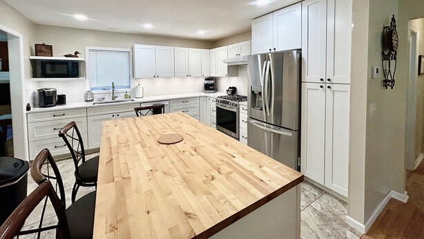 A kitchen with white cabinets, a stainless steel refrigerator, a wooden dining table, and a built-in oven. - Sprawling ranch W/ HUGE Yard, Patio, & W/D (Wichita)