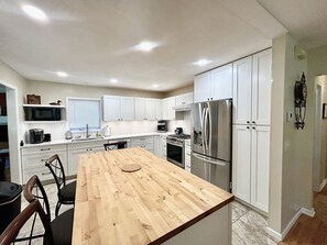 A kitchen with white cabinets, a stainless steel refrigerator, a wooden dining table, and a built-in oven. - Sprawling ranch W/ HUGE Yard, Patio, & W/D (Wichita)