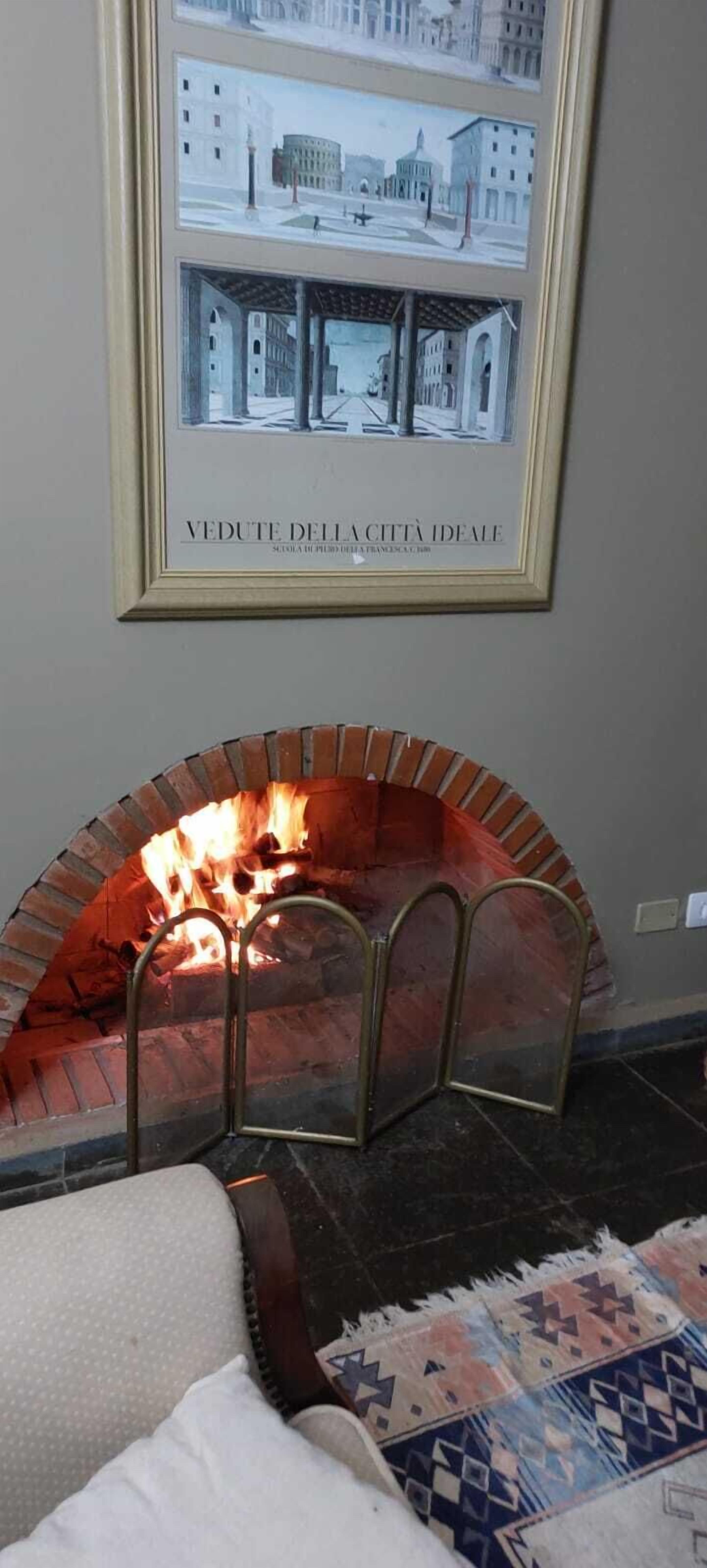 A framed architectural drawing above a brick fireplace with metal railings.