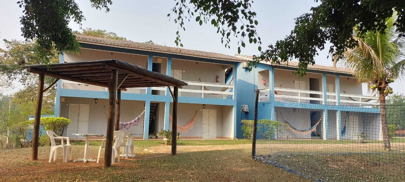 A two-story building with a blue and white exterior, a covered seating area with plastic chairs, and a hammock.