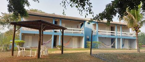 A two-story building with a blue and white exterior, a covered seating area with plastic chairs, and a hammock.