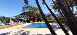 A pool area with lounge chairs and umbrellas, surrounded by palm trees and a small bar.