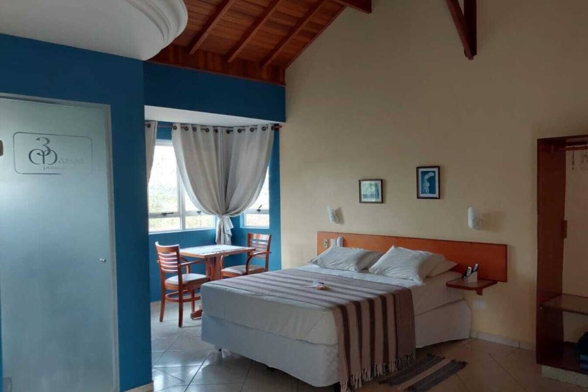 A bedroom with a bed, a nightstand, a chair, a table, and a window with curtains.