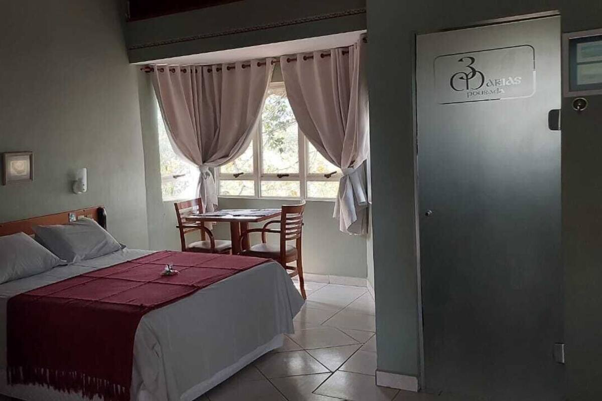 A bedroom with a bed, a desk, and a chair. There is a window with curtains and a door with a logo.