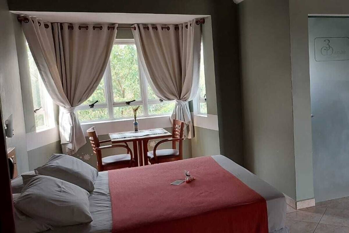 A bedroom with a bed, a desk, two doors, and a bathroom area with a sink and towel rack.