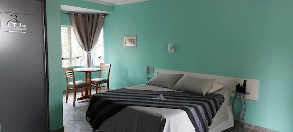 A room with a bed, a table with chairs, a window with curtains, and a door with a sign. - POUSADA 3 MARIAS (São Pedro)