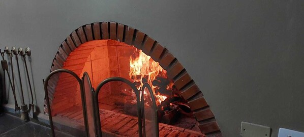 A brick oven with a fire burning inside, surrounded by metal railings.