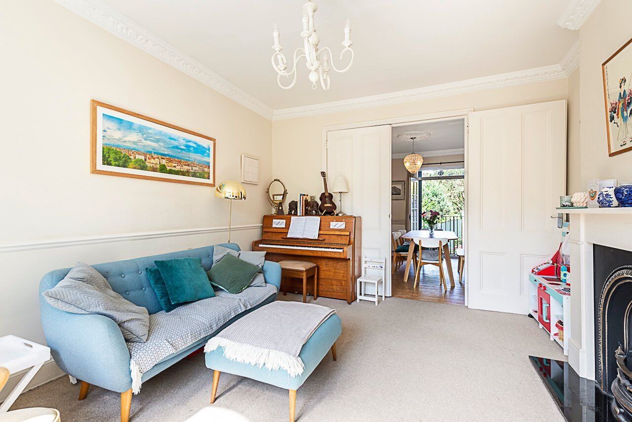 A living room with a blue sofa, a piano, a chandelier, and a painting on the wall.