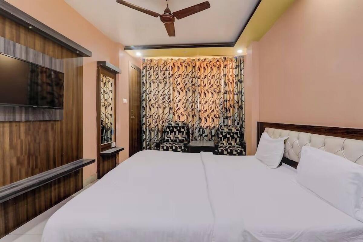 Un dormitorio con una cama grande, un ventilador de techo, un televisor montado en la pared y cortinas estampadas.