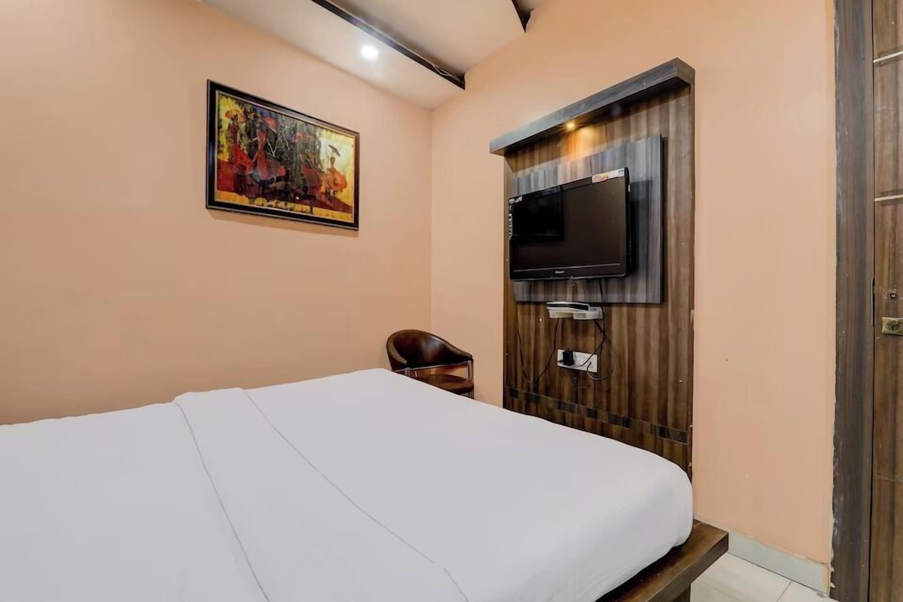 A bedroom with a bed, a TV mounted on the wall, a chair, and a painting.
