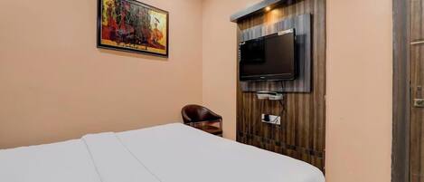 A bedroom with a bed, a TV mounted on the wall, a chair, and a painting.