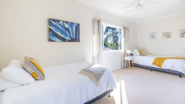 A bedroom with two beds, a ceiling fan, and a window with curtains.