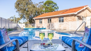 Un espace aménagé au bord de la piscine avec deux chaises longues, une table sur laquelle sont posés des verres de champagne et une piscine.