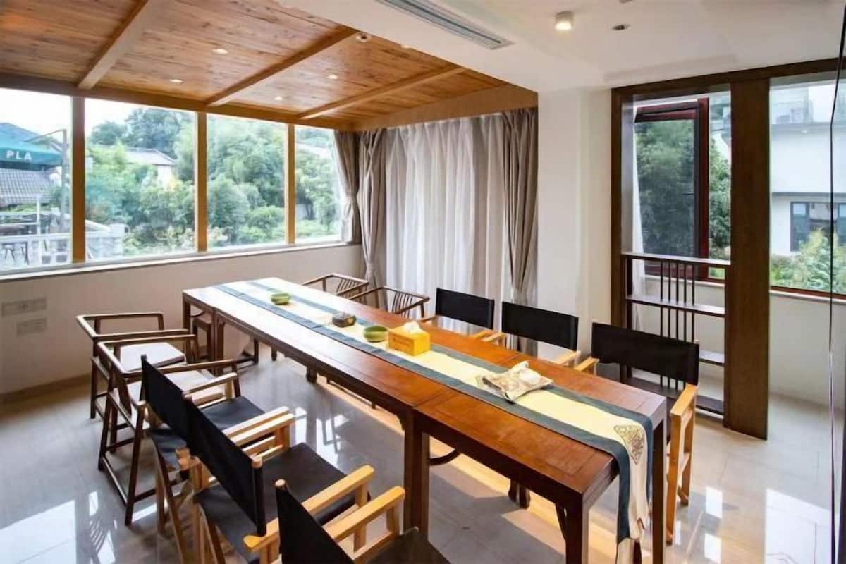 A modern dining area with a long wooden table, chairs, and large windows with curtains.