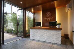 Un mostrador de recepción con un televisor, un letrero con el nombre 'TEAVILLA' y una planta en maceta.