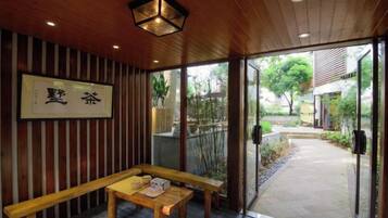 A traditional Japanese interior with a wooden bench and table, a framed calligraphy piece, and a view of the outside.