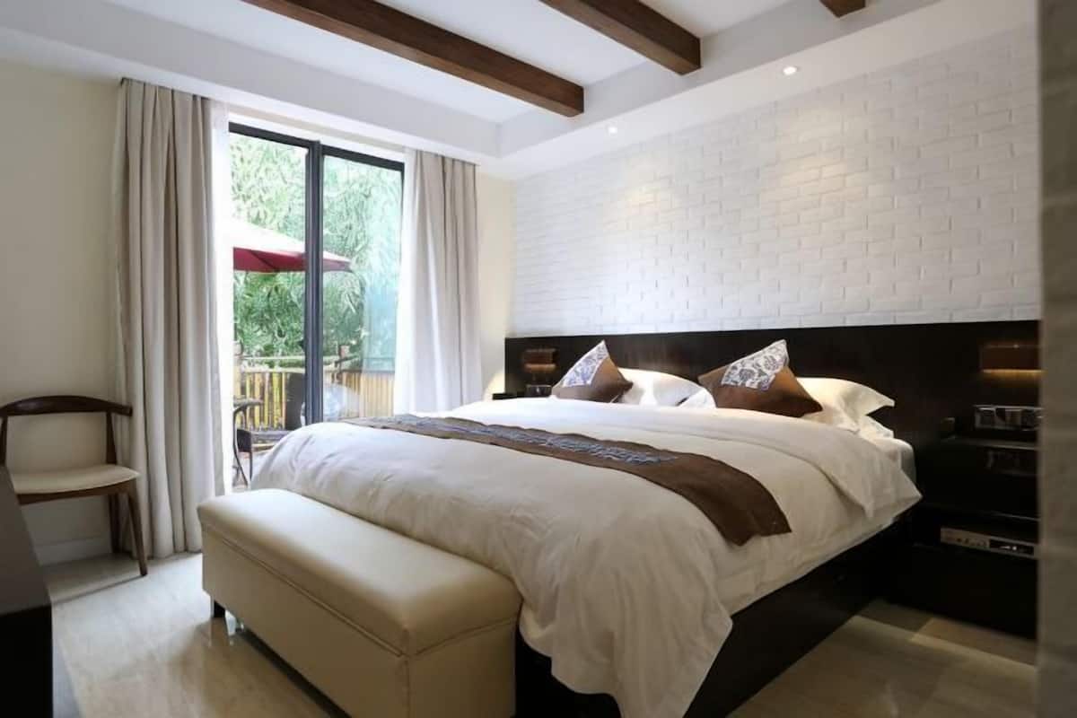 A bedroom with a large bed, a bench, a chair, and a view of the outdoors.