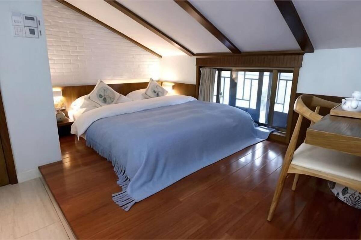 A bedroom with a bed, wooden floor, a nightstand, a chair, and a window with curtains.
