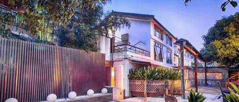 A modern two-story house with a balcony, a wooden fence, and a landscaped garden with spherical planters.