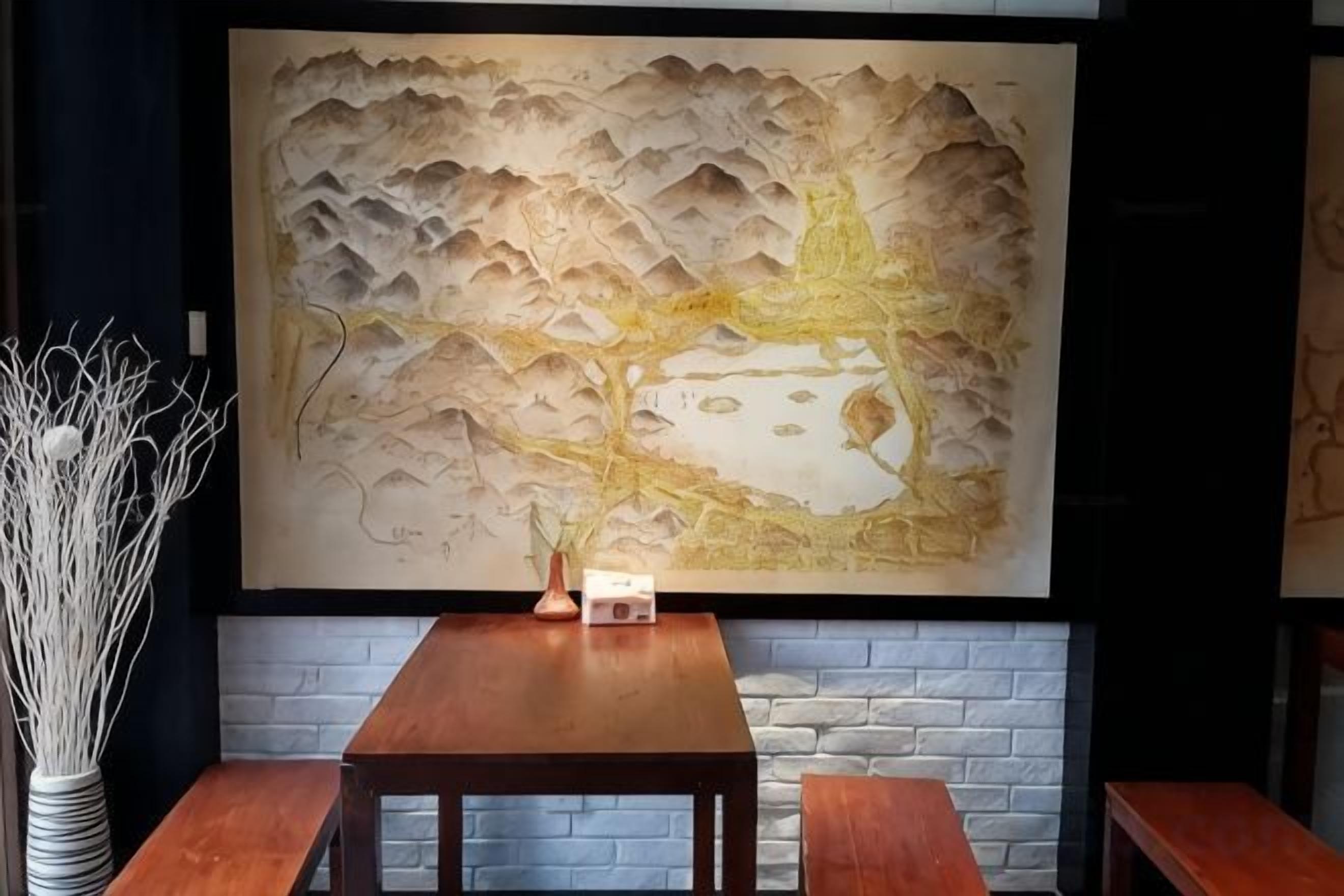 A dining area with a wooden table and benches, a vase with branches, and a large wall mural.