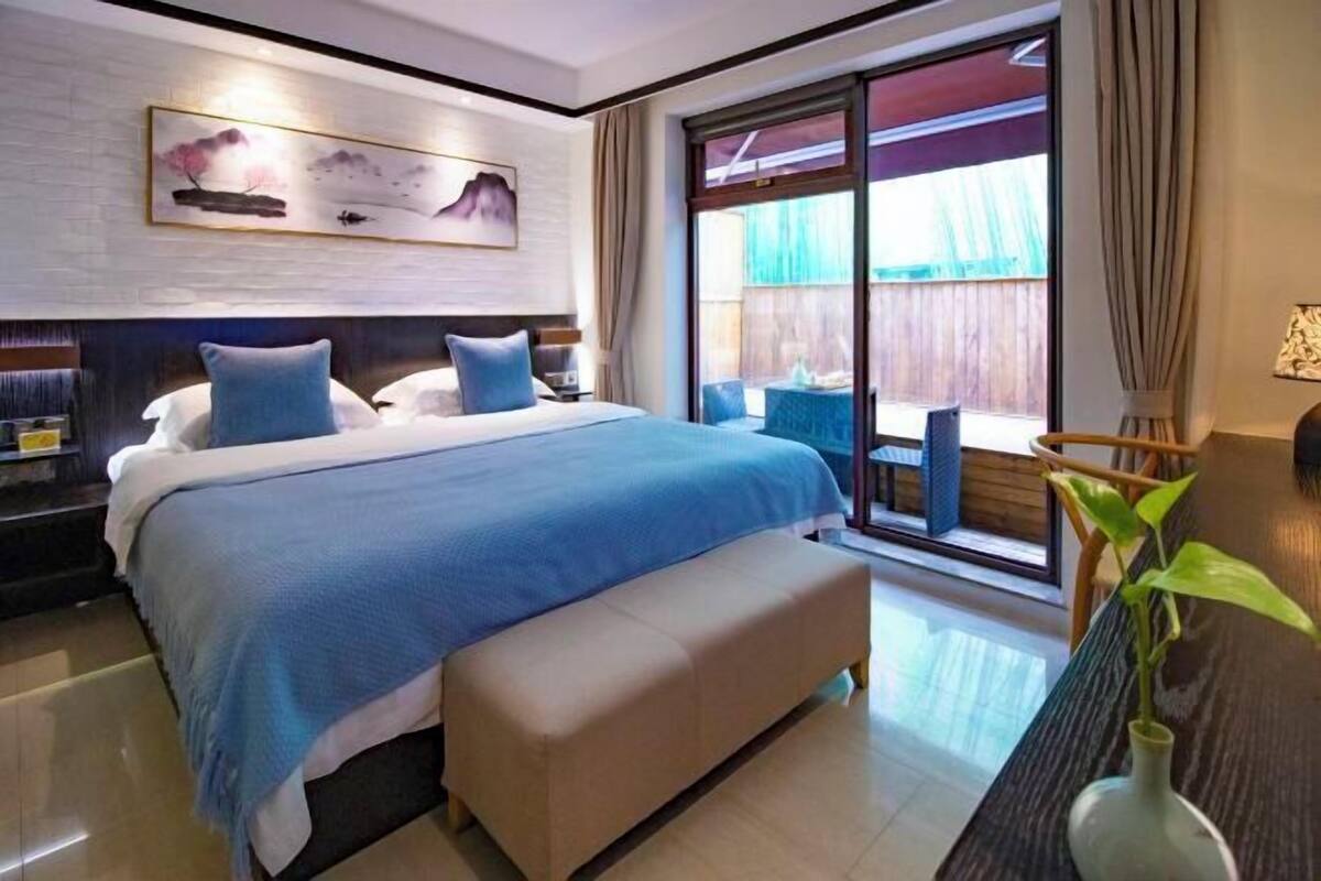 A bedroom with a large bed, a bench, a desk, and a sliding glass door leading to an outdoor area.