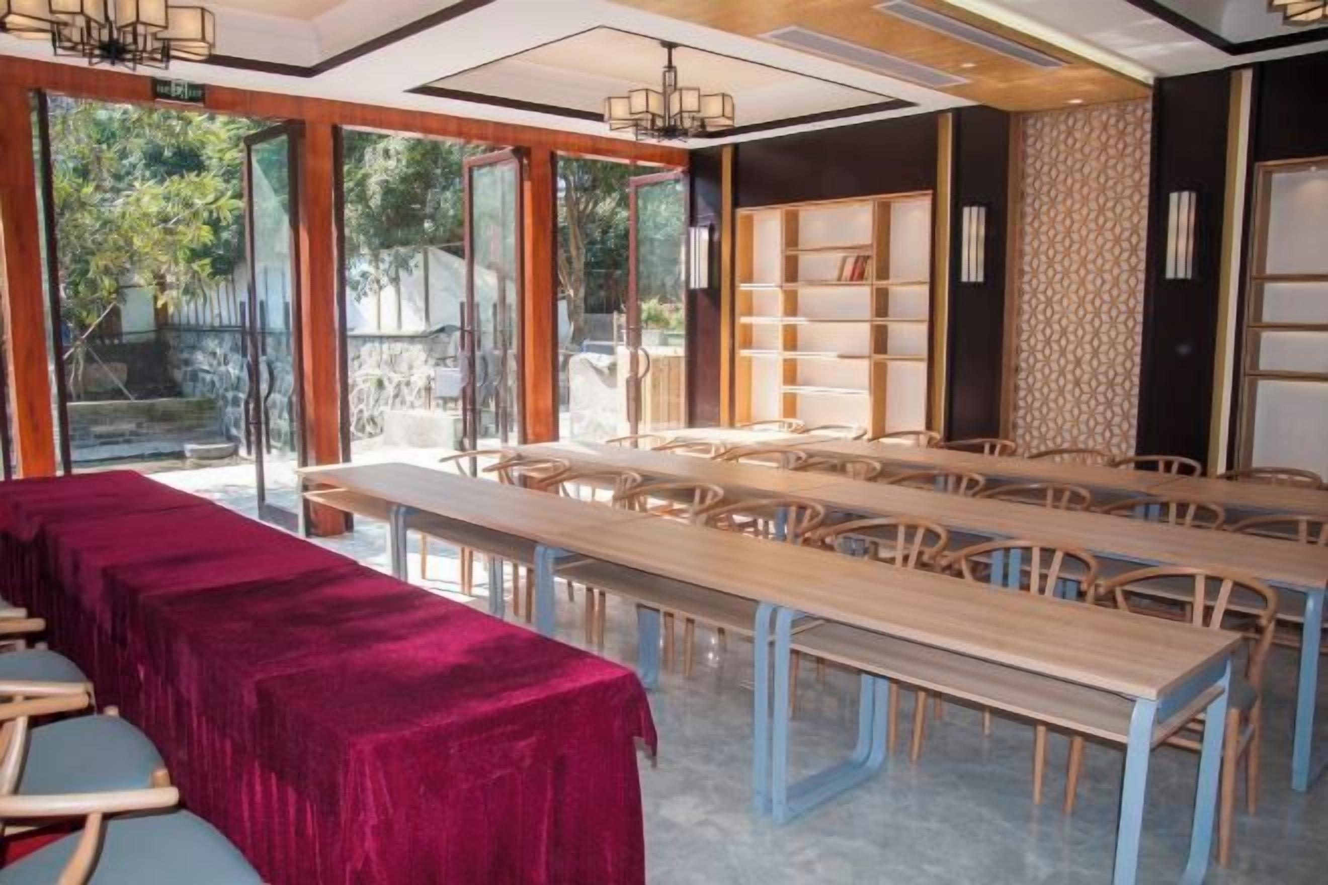 Una sala da pranzo con lunghi tavoli e sedie, una tovaglia rossa e una libreria.