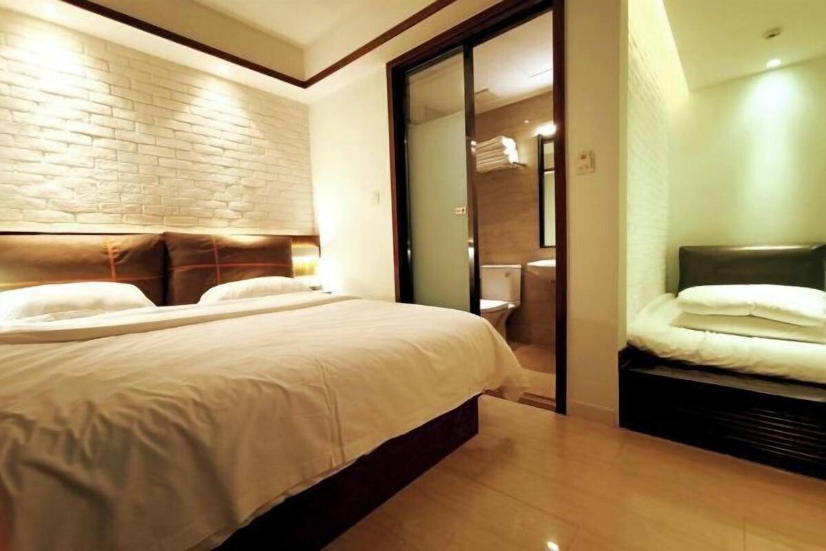 A hotel room with a large bed, a sliding door to a bathroom, and a brick-patterned wall.