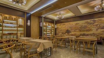 Un comedor con mesas y sillas, una pared con un mural, y estantes con objetos a la izquierda.